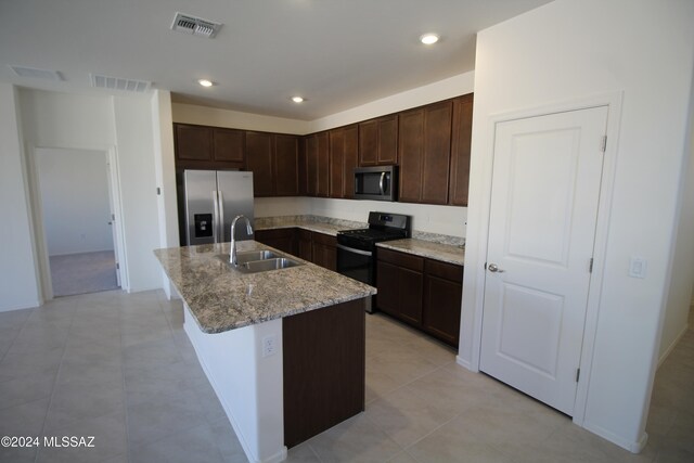 kitchen featuring sink, an island with sink, light stone countertops, dark brown cabinets, and appliances with stainless steel finishes