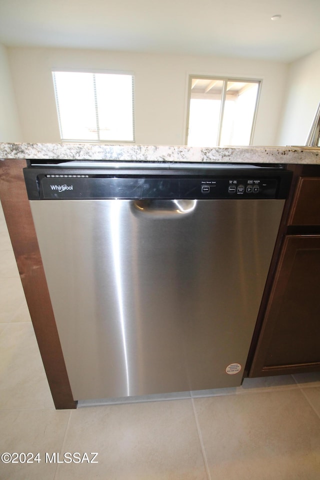 details featuring dark brown cabinetry, light stone countertops, light tile patterned floors, and dishwasher