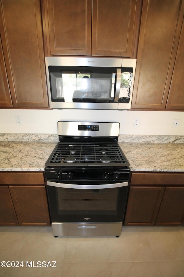 kitchen featuring stainless steel appliances, light tile patterned flooring, and light stone counters