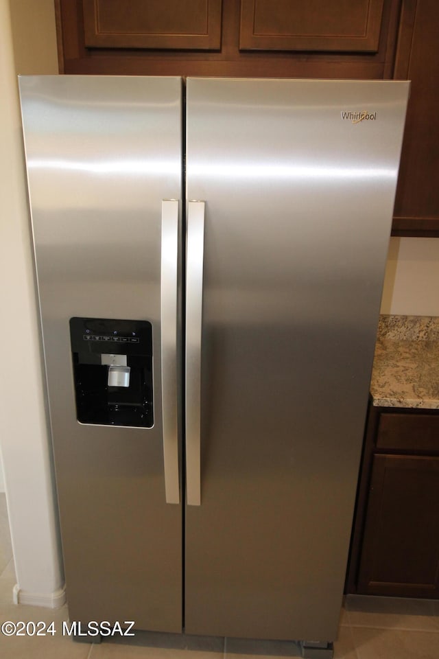 room details with light stone counters, stainless steel fridge with ice dispenser, dark brown cabinets, and light tile patterned flooring