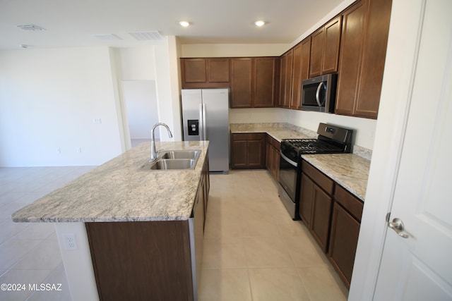 kitchen with light stone counters, appliances with stainless steel finishes, light tile patterned floors, sink, and a kitchen island with sink