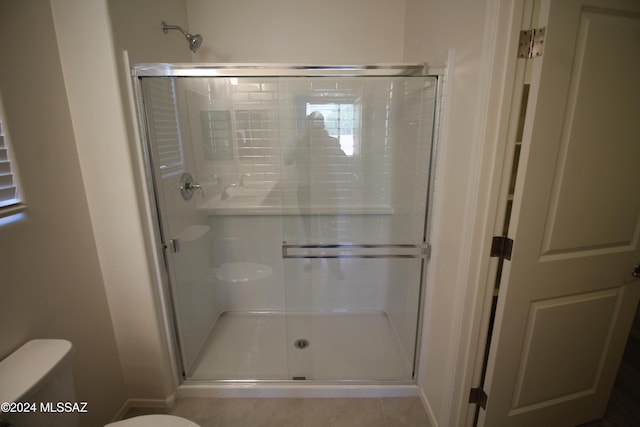 bathroom featuring toilet, an enclosed shower, and tile patterned floors