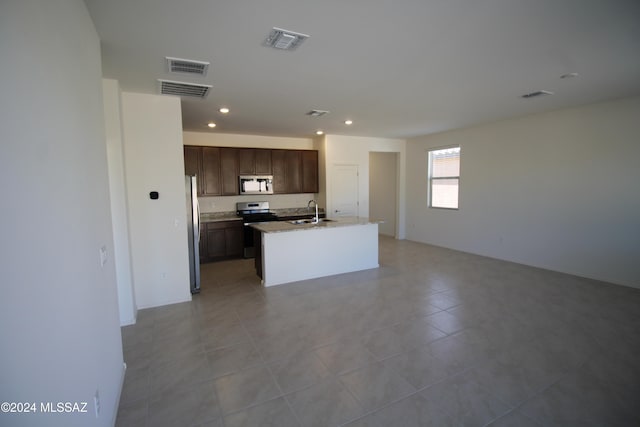 kitchen featuring a center island with sink, dark brown cabinetry, sink, light tile patterned flooring, and appliances with stainless steel finishes