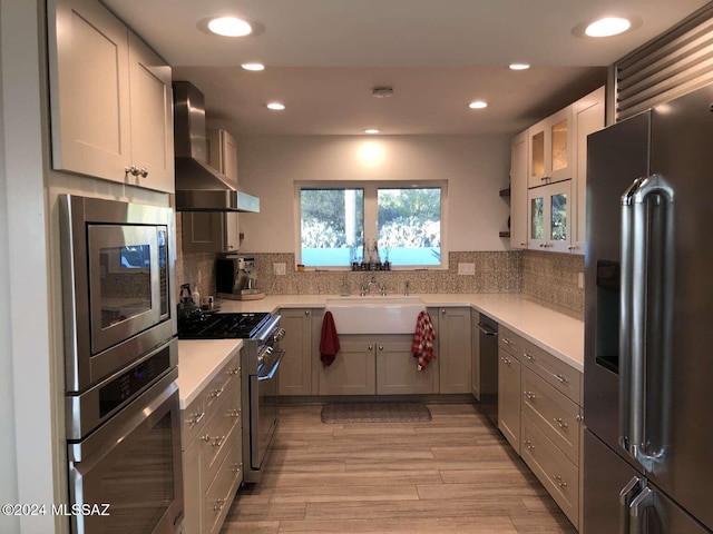 kitchen with wall chimney range hood, high quality appliances, light hardwood / wood-style flooring, sink, and gray cabinets