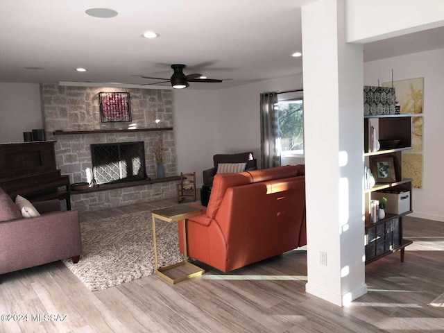 living room featuring a stone fireplace, wood-type flooring, and ceiling fan