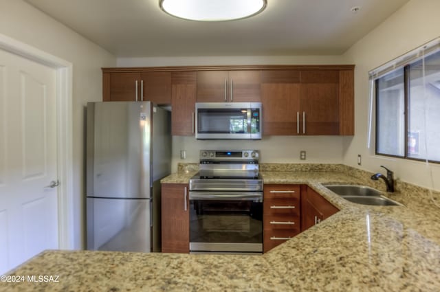 kitchen with stainless steel appliances, light stone countertops, and sink