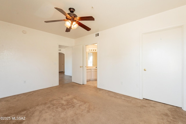 unfurnished bedroom featuring visible vents, ceiling fan, light colored carpet, arched walkways, and ensuite bath