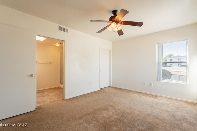 unfurnished bedroom with visible vents, baseboards, light colored carpet, a ceiling fan, and ensuite bath