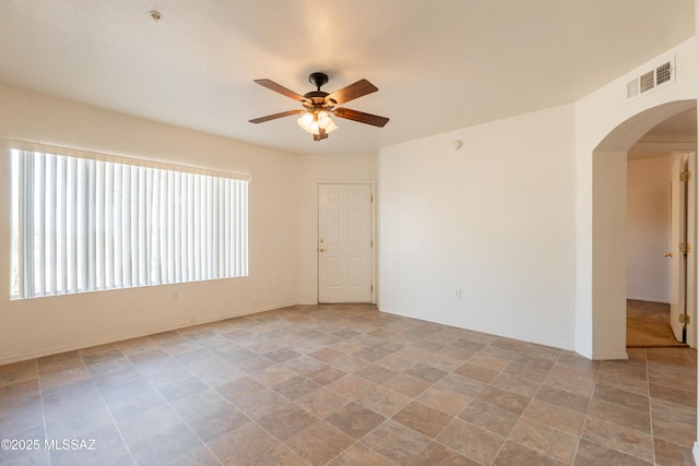 spare room with visible vents, arched walkways, stone finish flooring, and ceiling fan