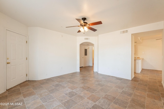 spare room with visible vents, a ceiling fan, arched walkways, and stone finish floor
