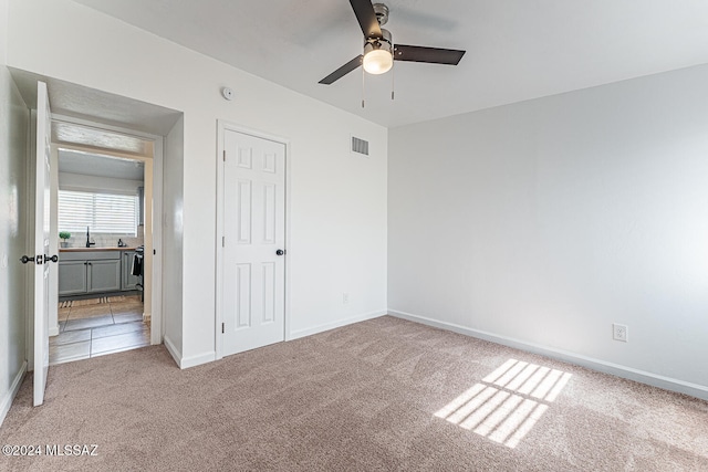 unfurnished bedroom featuring ceiling fan, a closet, light colored carpet, and sink