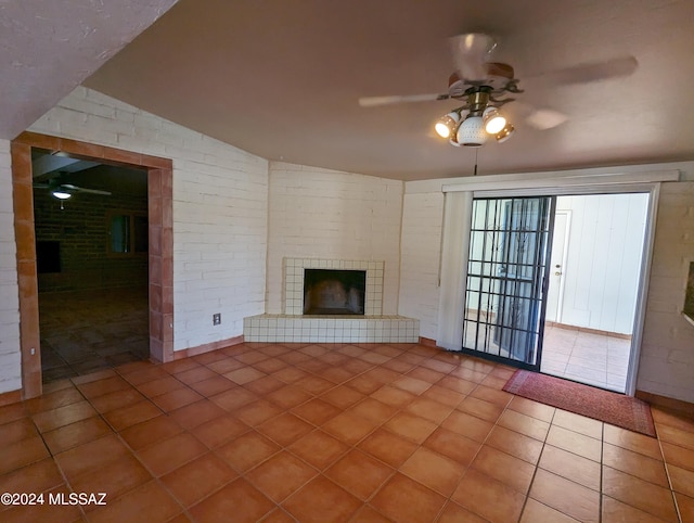 unfurnished living room featuring tile patterned floors, vaulted ceiling, ceiling fan, a fireplace, and brick wall