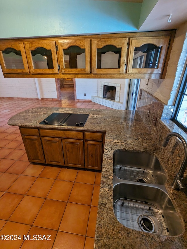 kitchen featuring light tile patterned flooring, a fireplace, sink, dark stone countertops, and black electric cooktop