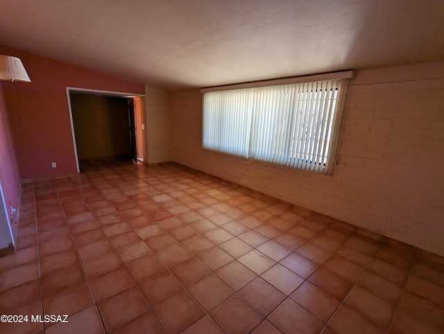 unfurnished room featuring vaulted ceiling and brick wall