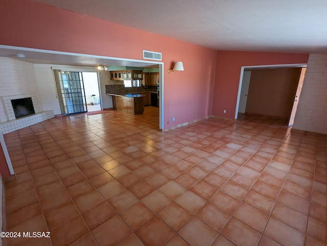 unfurnished living room featuring lofted ceiling, light tile patterned floors, and a fireplace