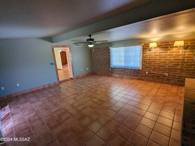 tiled empty room with beamed ceiling, brick wall, and ceiling fan