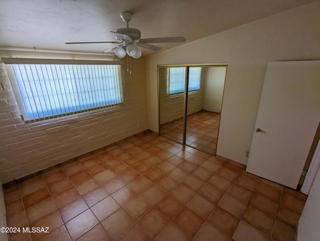 unfurnished bedroom featuring ceiling fan, multiple windows, a closet, and brick wall