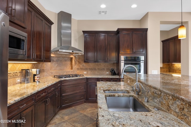 kitchen with sink, wall chimney exhaust hood, appliances with stainless steel finishes, tasteful backsplash, and decorative light fixtures