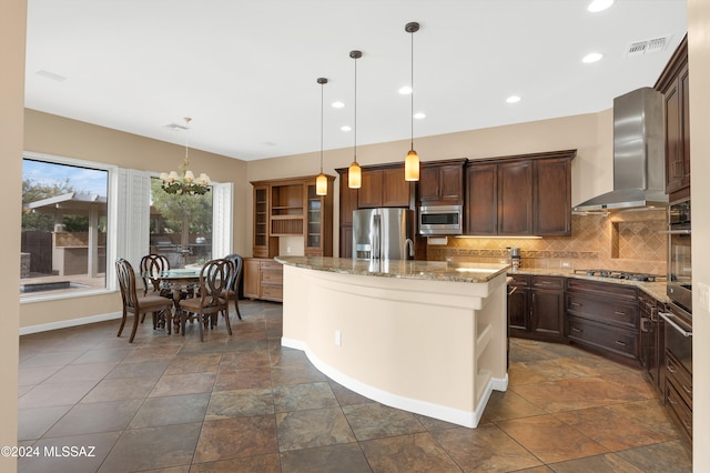 kitchen with a center island, wall chimney range hood, light stone countertops, decorative light fixtures, and stainless steel appliances