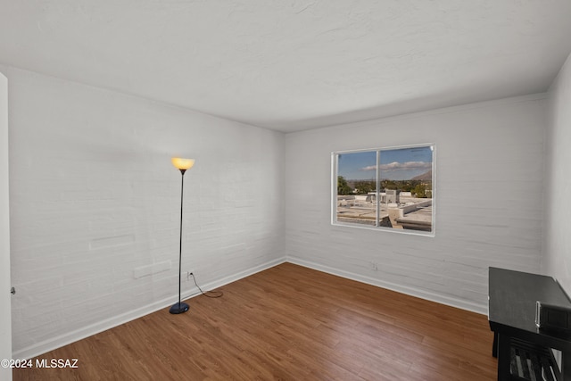 unfurnished room featuring hardwood / wood-style floors and brick wall