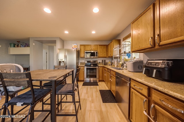 kitchen featuring light hardwood / wood-style floors, light stone countertops, sink, and appliances with stainless steel finishes