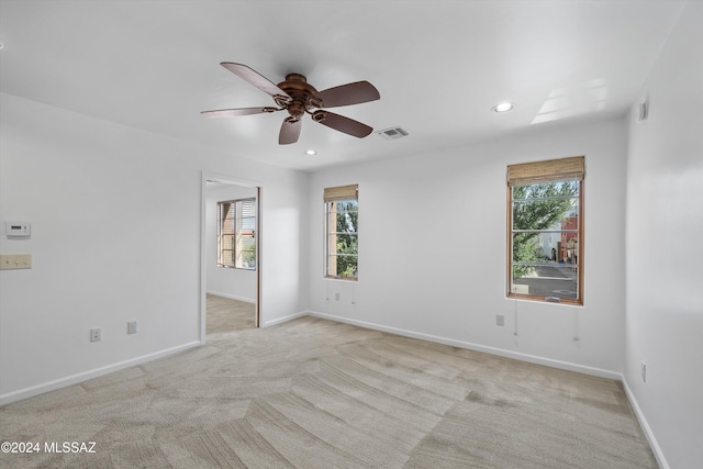 spare room with a wealth of natural light, light carpet, and ceiling fan