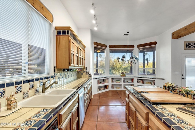 kitchen featuring sink, stainless steel dishwasher, tile countertops, pendant lighting, and a chandelier