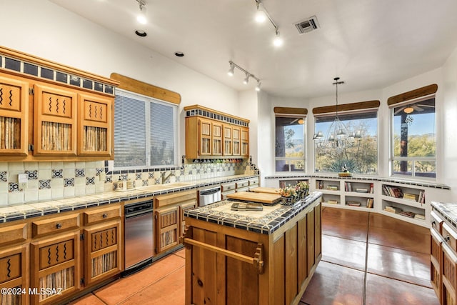 kitchen with tile countertops, backsplash, sink, hanging light fixtures, and a kitchen island