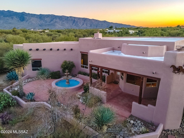 back of property at dusk with a patio area, a mountain view, and stucco siding