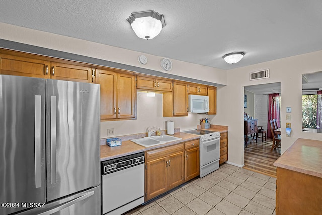 kitchen with a textured ceiling, sink, light tile patterned floors, and white appliances