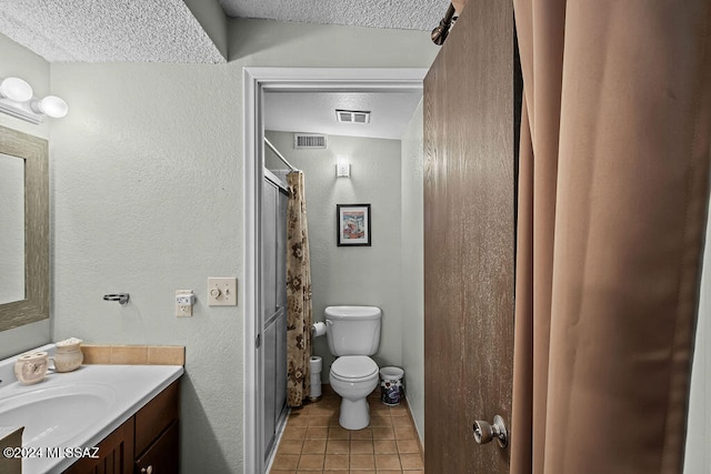 bathroom featuring toilet, tile patterned flooring, vanity, a textured ceiling, and walk in shower