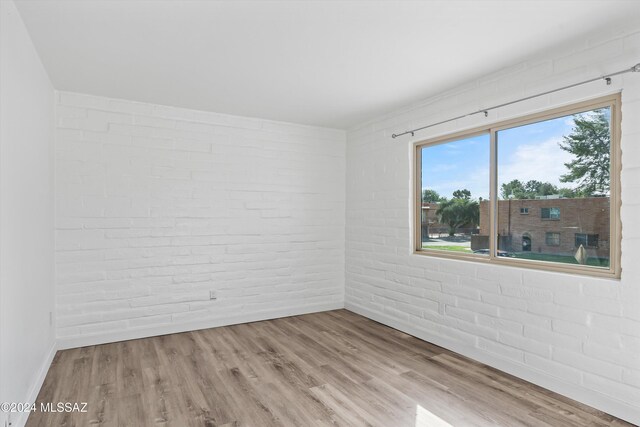 unfurnished room with brick wall and light wood-type flooring