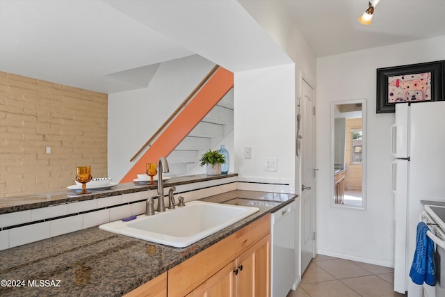 kitchen with dark stone counters, sink, light tile patterned flooring, light brown cabinetry, and white appliances