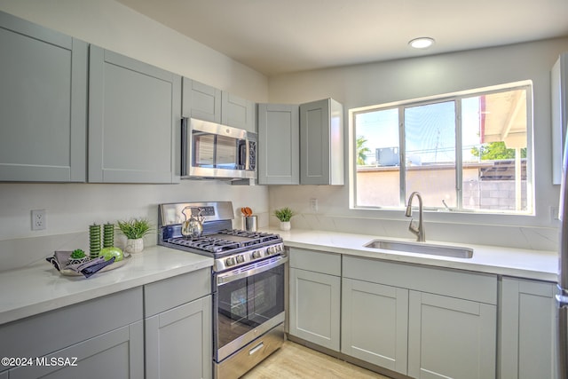 kitchen with gray cabinets, appliances with stainless steel finishes, sink, and light hardwood / wood-style floors