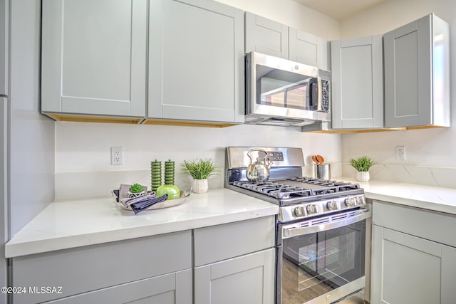 kitchen featuring gray cabinets, appliances with stainless steel finishes, hardwood / wood-style floors, and light stone counters