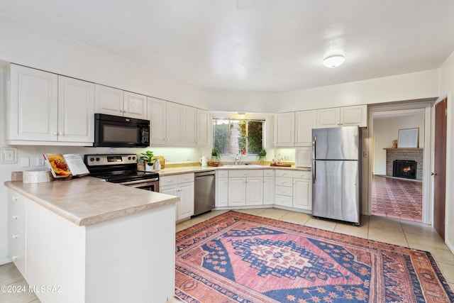 kitchen with white cabinetry, stainless steel appliances, a brick fireplace, kitchen peninsula, and light tile patterned floors