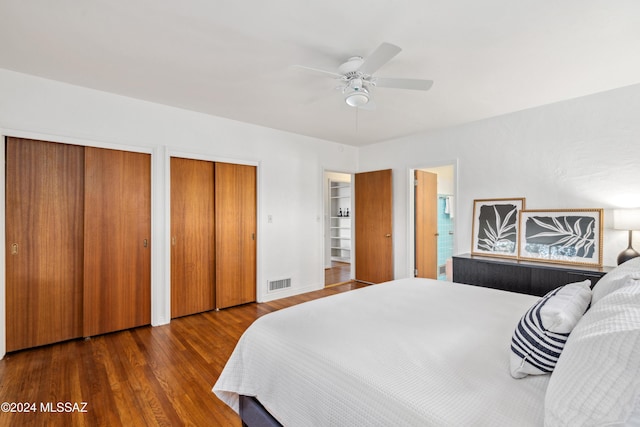 bedroom with dark hardwood / wood-style flooring, ceiling fan, and multiple closets