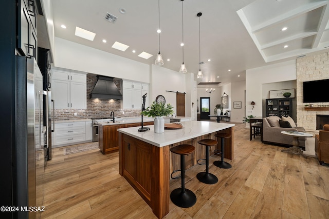 kitchen with a barn door, light hardwood / wood-style floors, a spacious island, white cabinets, and custom exhaust hood