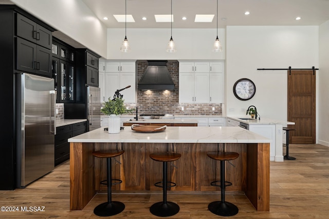 kitchen featuring a spacious island, custom range hood, a barn door, appliances with stainless steel finishes, and glass insert cabinets