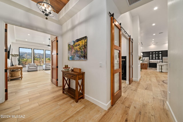 hall with baseboards, a barn door, a towering ceiling, and light wood-style floors