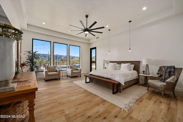 bedroom featuring ceiling fan, light hardwood / wood-style floors, a mountain view, and a tray ceiling