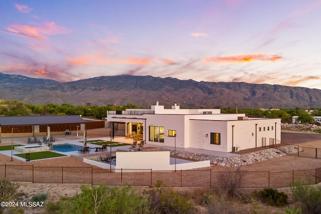 back house at dusk with a mountain view, a patio, and a fenced in pool