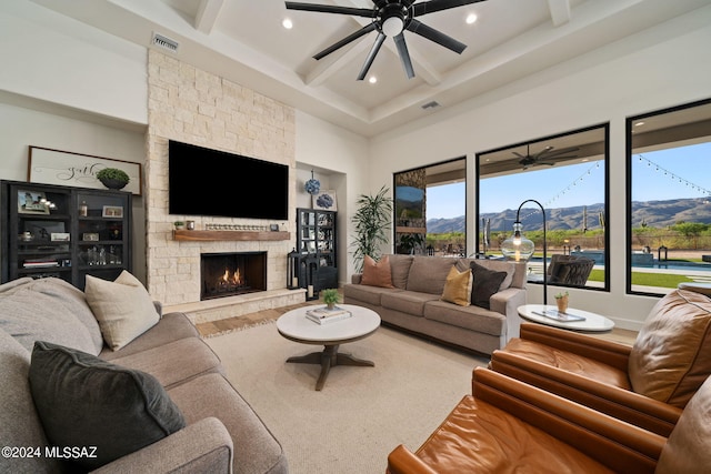 living room with ceiling fan, a fireplace, beamed ceiling, and a high ceiling