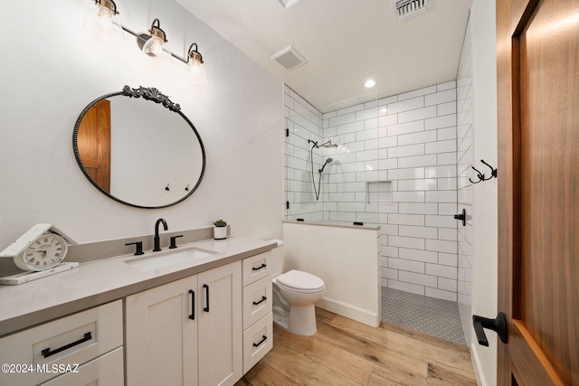 bathroom featuring a tile shower, hardwood / wood-style floors, vanity, and toilet