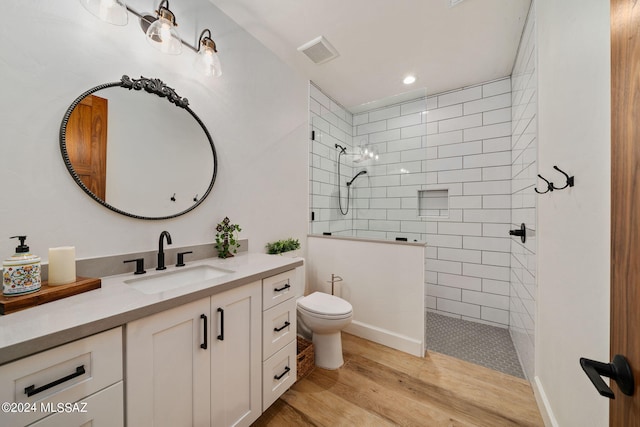 bathroom with hardwood / wood-style flooring, toilet, a tile shower, and vanity