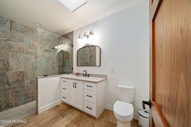 bathroom with a skylight, baseboards, wood finished floors, walk in shower, and vanity