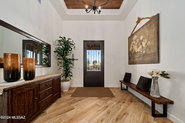 foyer entrance with a raised ceiling, baseboards, a notable chandelier, and light wood finished floors