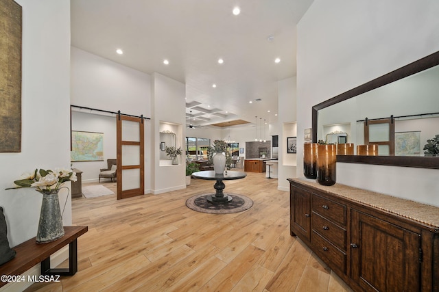 interior space with a towering ceiling, light wood-style floors, a barn door, and recessed lighting