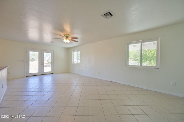 empty room featuring ceiling fan, a healthy amount of sunlight, light tile patterned floors, and french doors