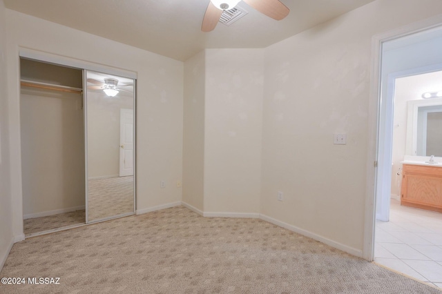 unfurnished bedroom featuring a closet, sink, light colored carpet, ceiling fan, and ensuite bathroom